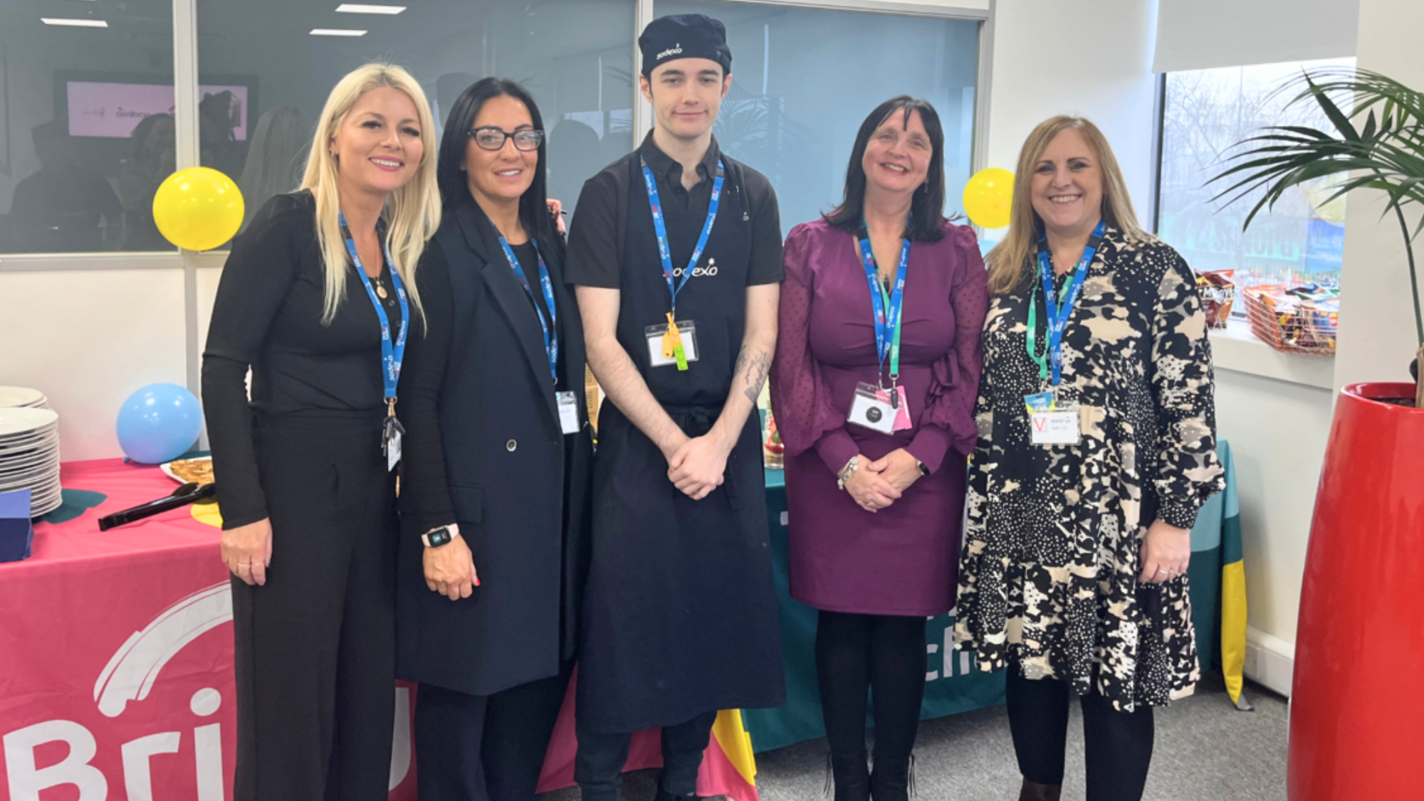 Bayleigh in his work uniform is stood in the middle of the supported internship team smiling at the camera