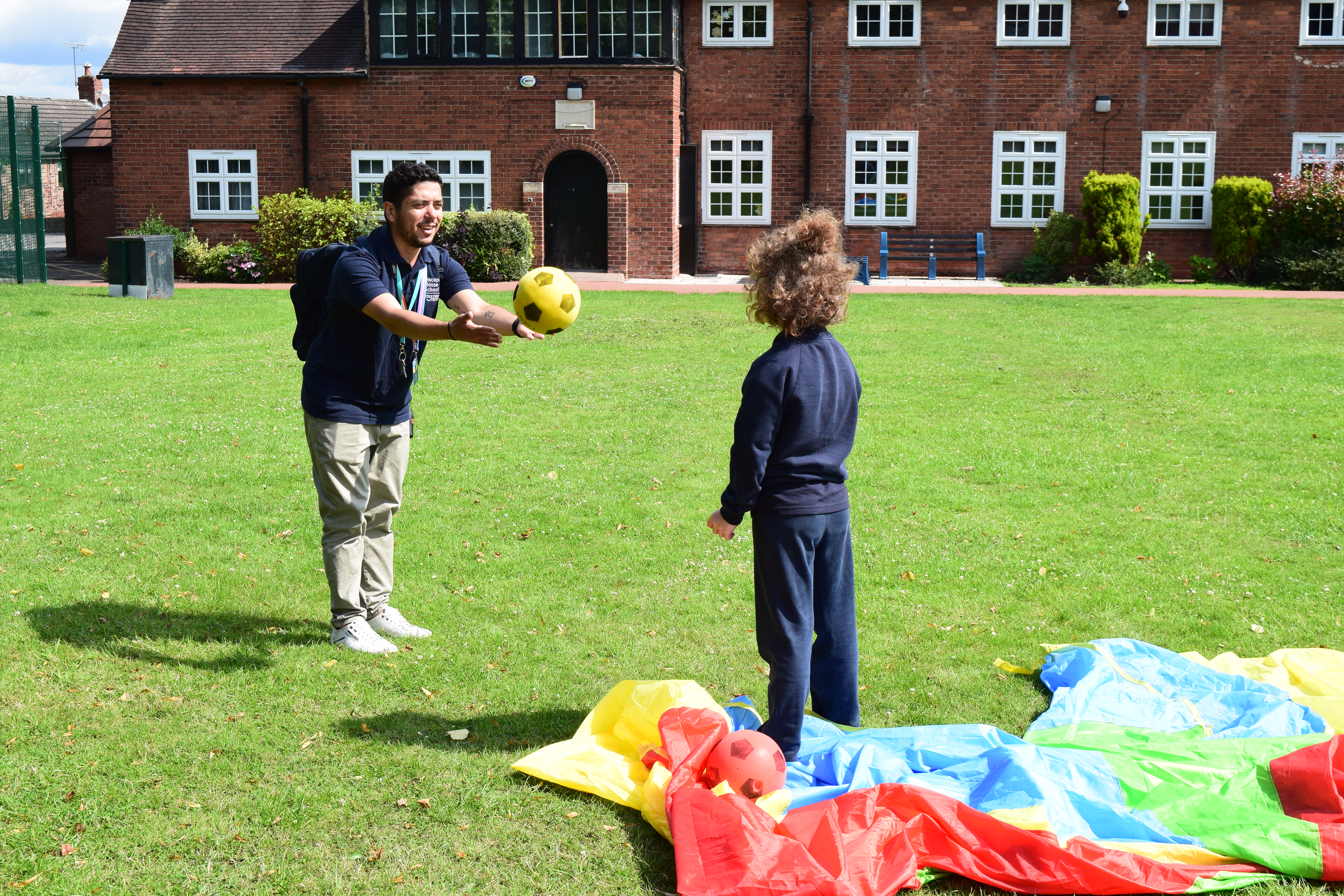 Staff member passing a ball to a student at the sports field.