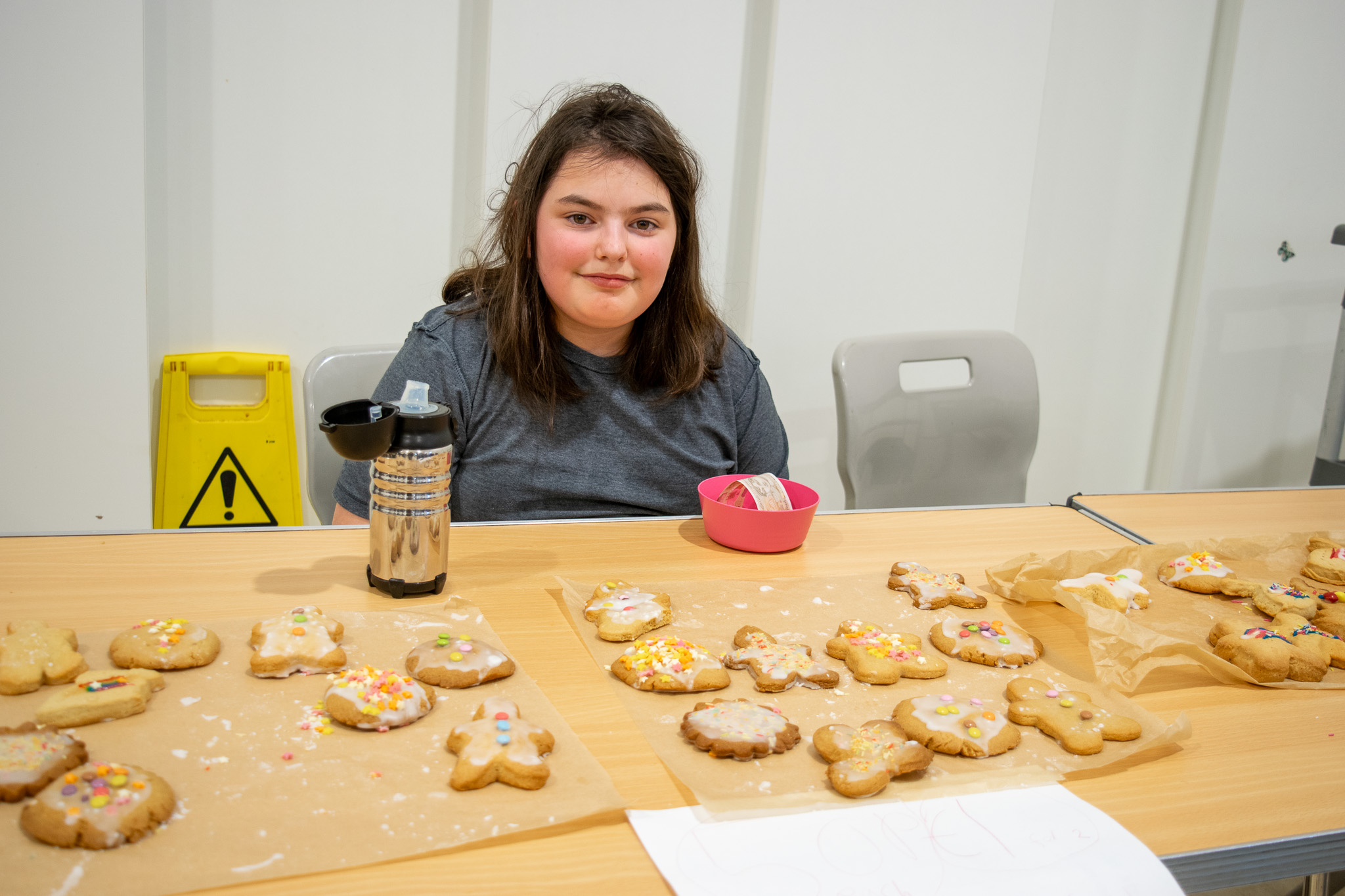 Student smiling behind a desk full of decorated gingerbread for sale. 