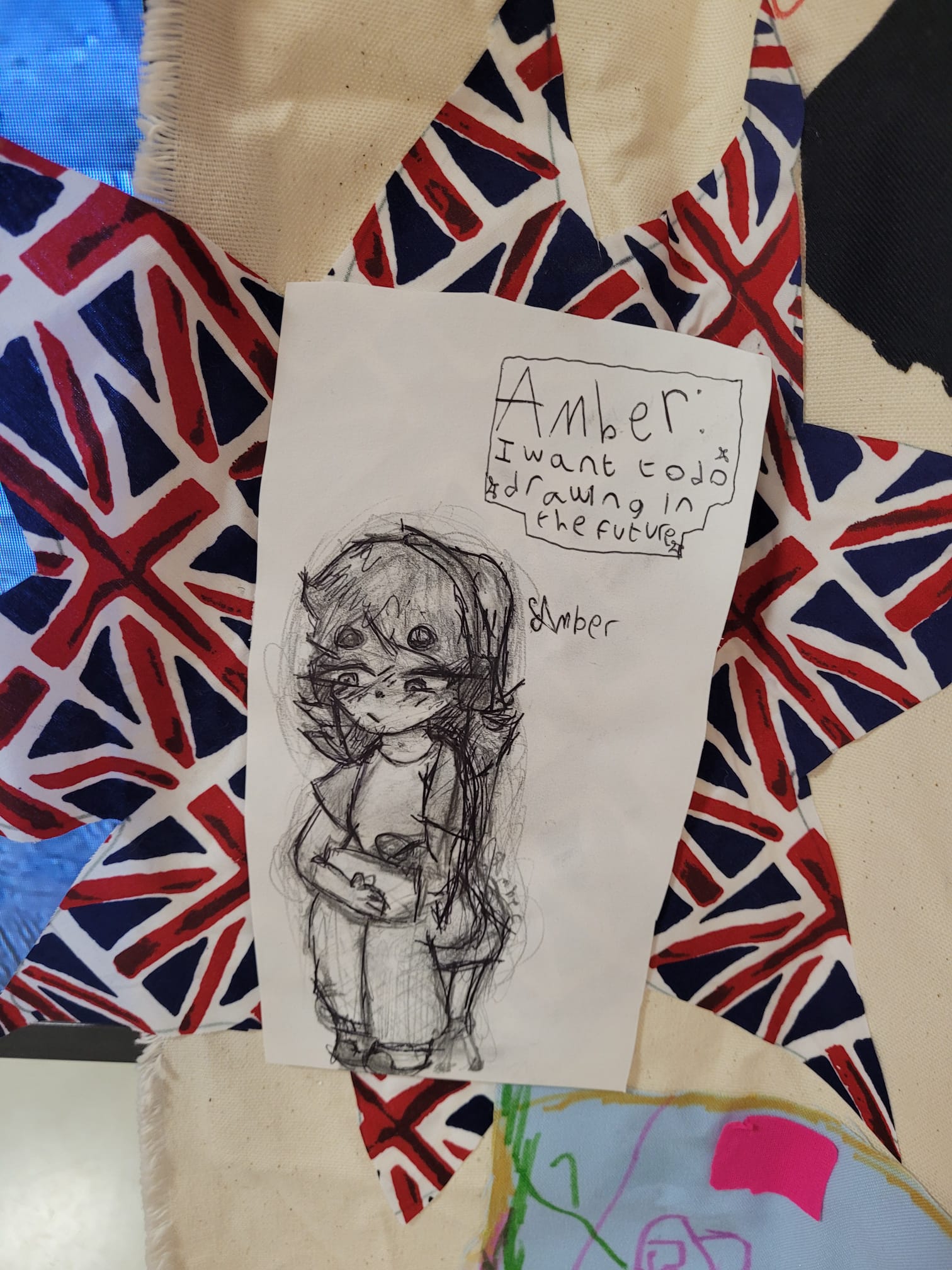 Black and white Pencil and pen drawing of a cartoon character. They are sat on a chair drawing and looking into the distance. To the left handwritten text "Amber: I want to do drawing in the future".
