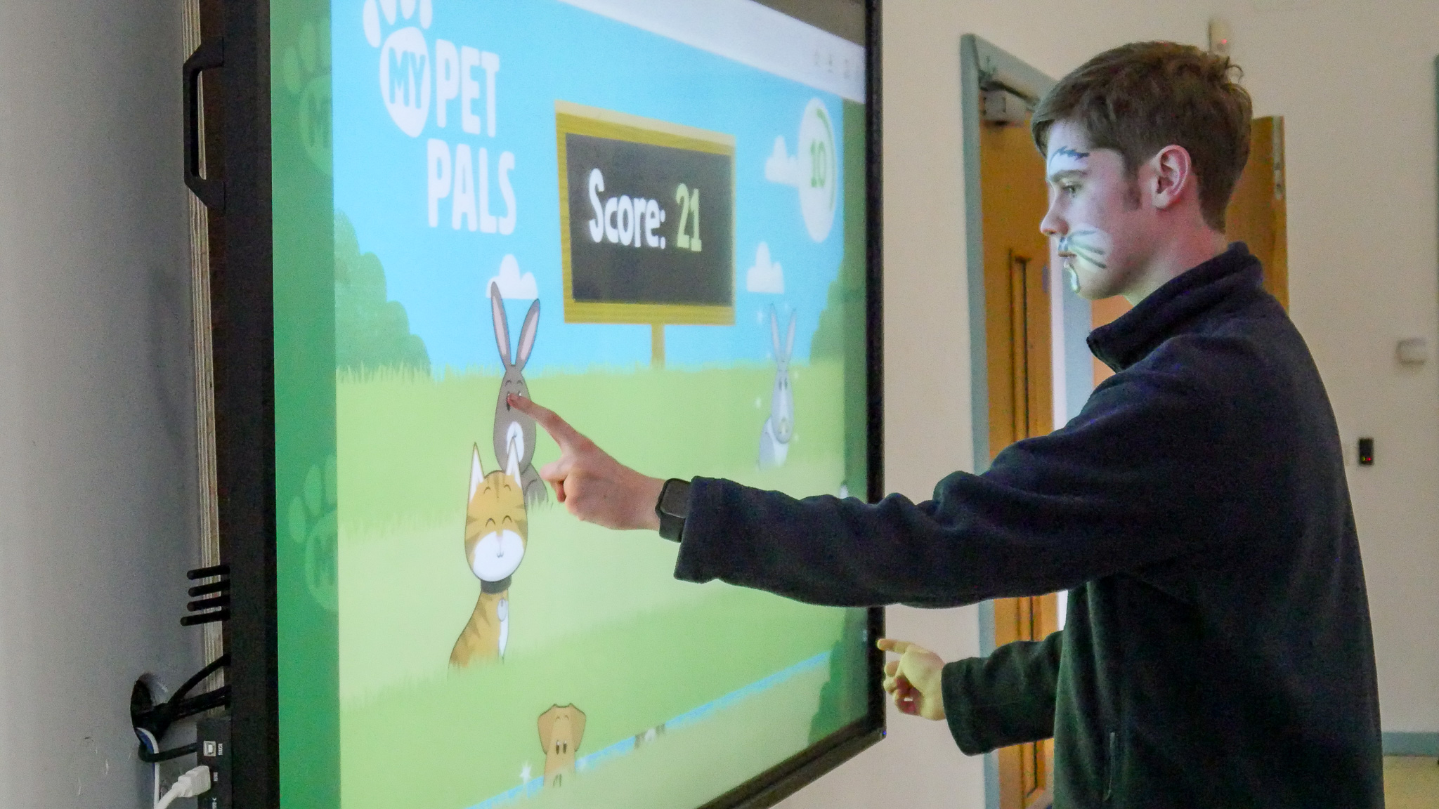 A student playing a video game on an interactive screen. His face is painted like a cat.