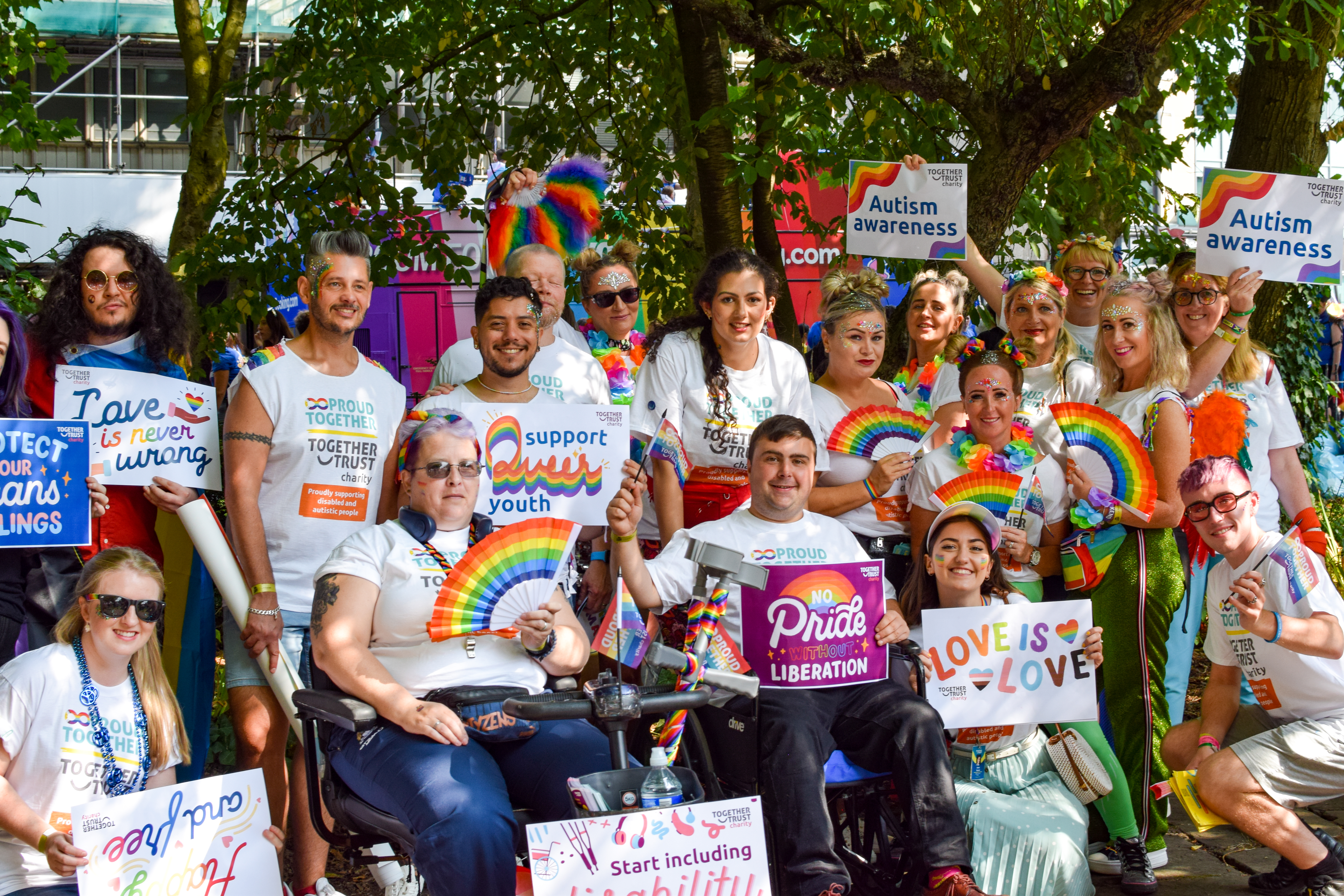 Group of people at pride parade dressed up in rainbow merch holding various signs with messages of support towards queer youth. 