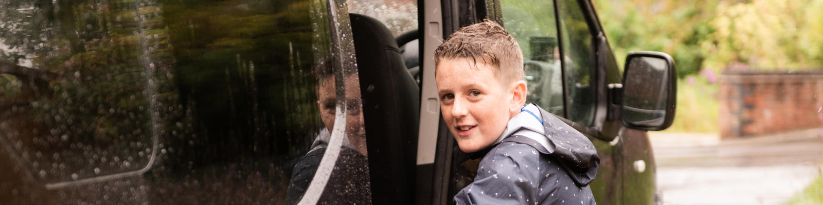 Young boy smiling at the camera as he is getting into a car. 