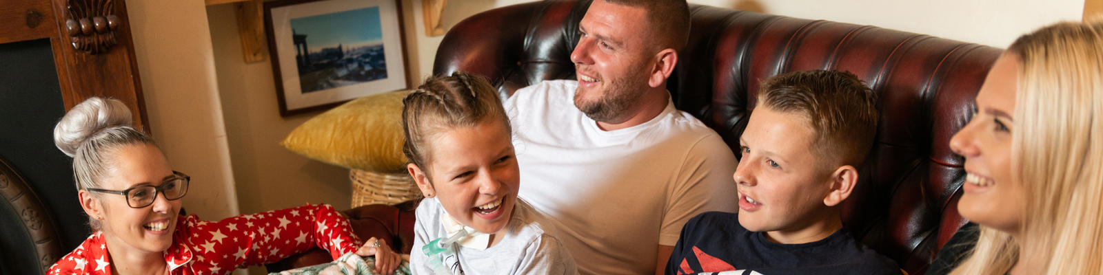 A group of people smiling wide at each other. They are all wearing pyjamas and lounging around the home. 