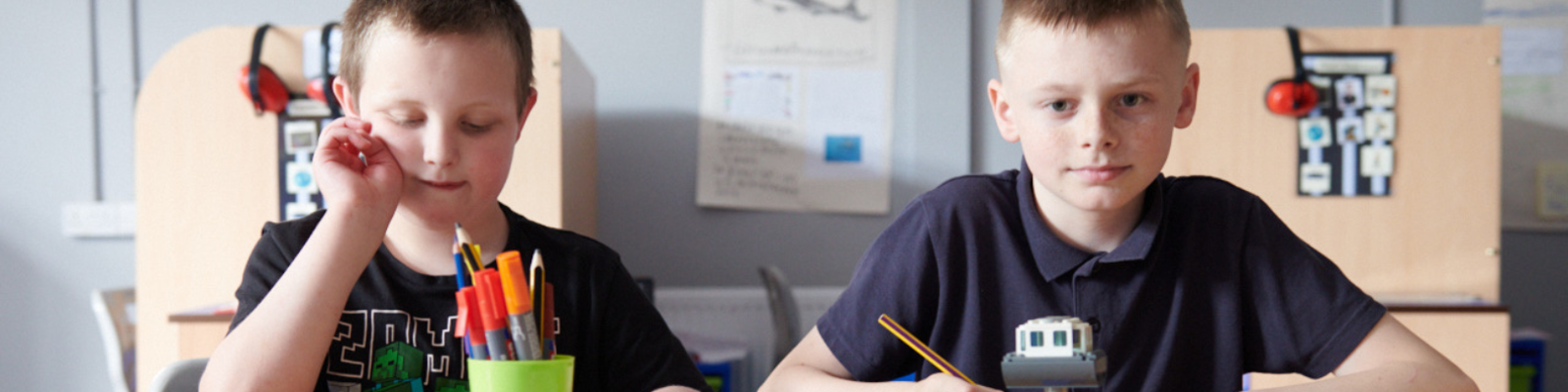 two young boys sitting next to each other at a desk in school working