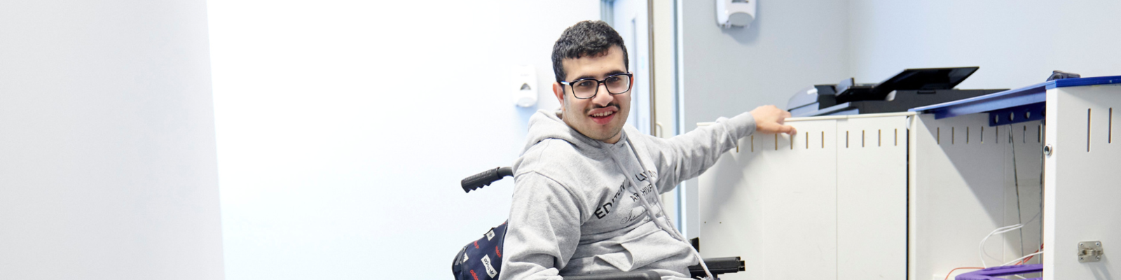 Man in wheelchair in front of an ipad charging station in the college hallway