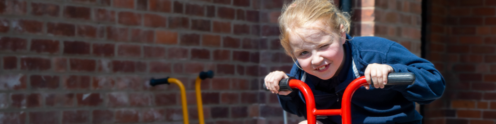 Young girl cycling on a red bike, she is winking at the camera as sun shines on her face