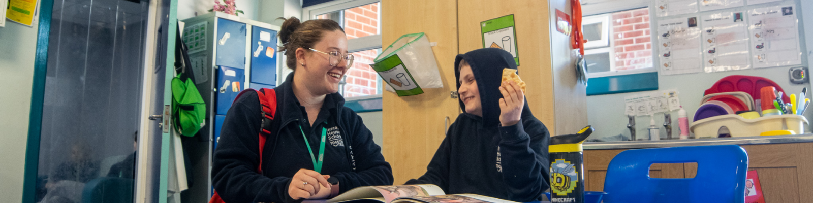 Young student is sat at a table laughing at his teacher. 