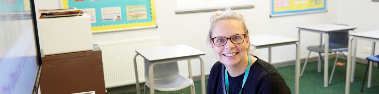 teacher wearing school jumper and lanyard smiling. 