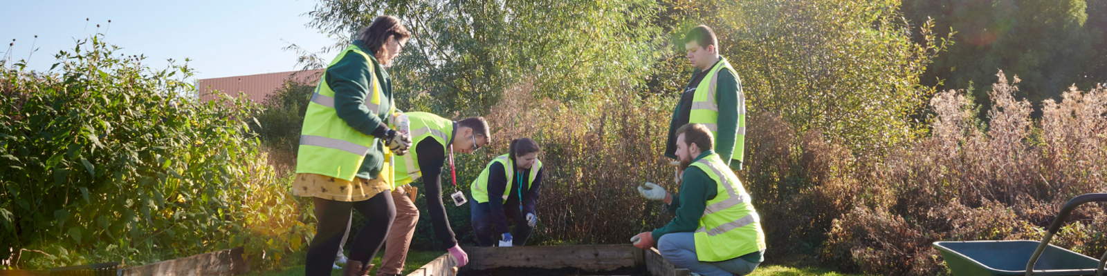 A group of students and the horticulture teacher gathered outside over a patch of vegetables. Some are crouching to plant seeds.