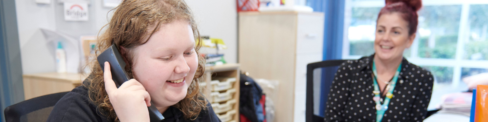 Smiling receptionist looking at student woman answering the phone at the reception desk.