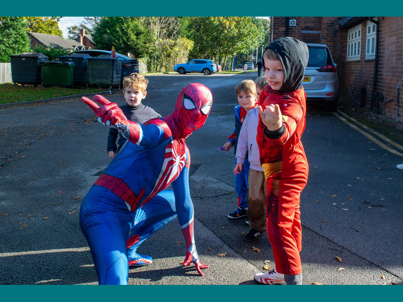 Spiderman poses on the ground showing a group of children how to 'shoot their webs'.