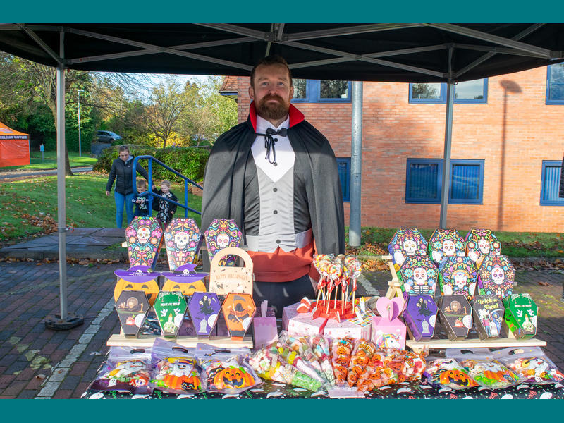 A vendor dressed as Dracula stands in front of his stall selling colourful treats.