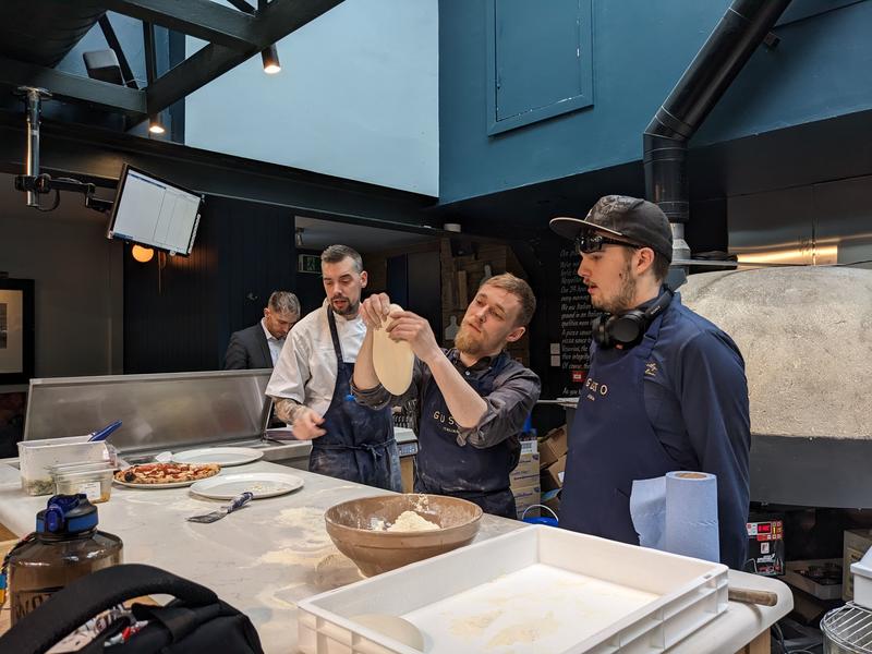 Mikey showing a student how to prepare the pizza dough.