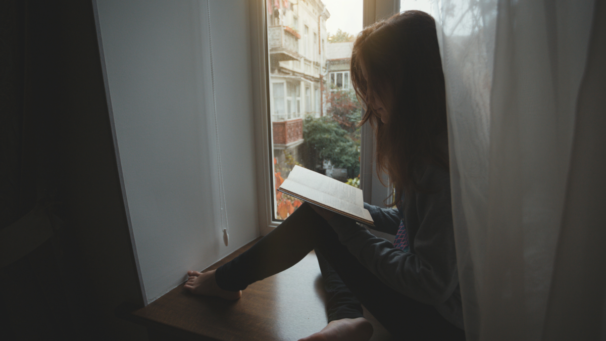 Young girl sitting in front of a window, reading.