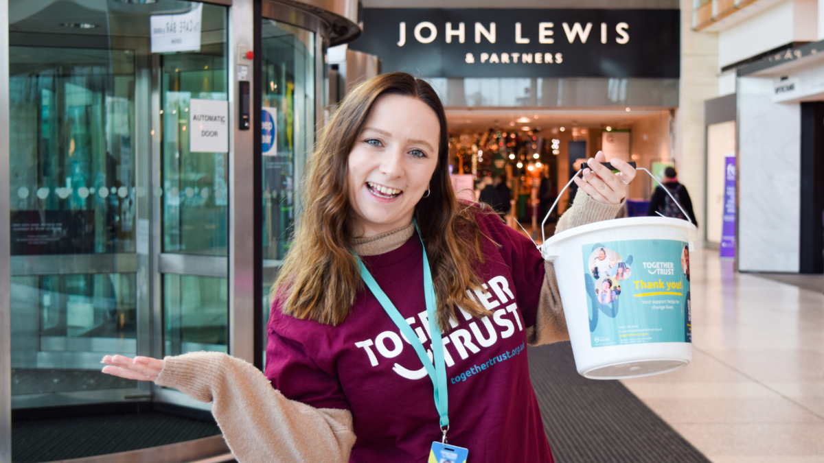 A staff member holding up a donation bucket in front of the john lewis store 