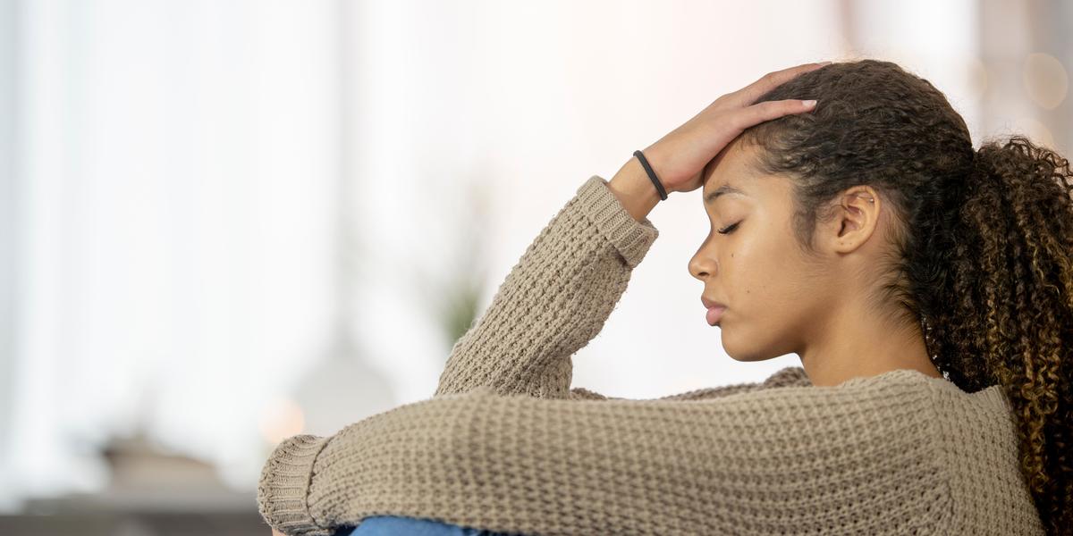 Young woman sitting and holding her head, looking stressed.