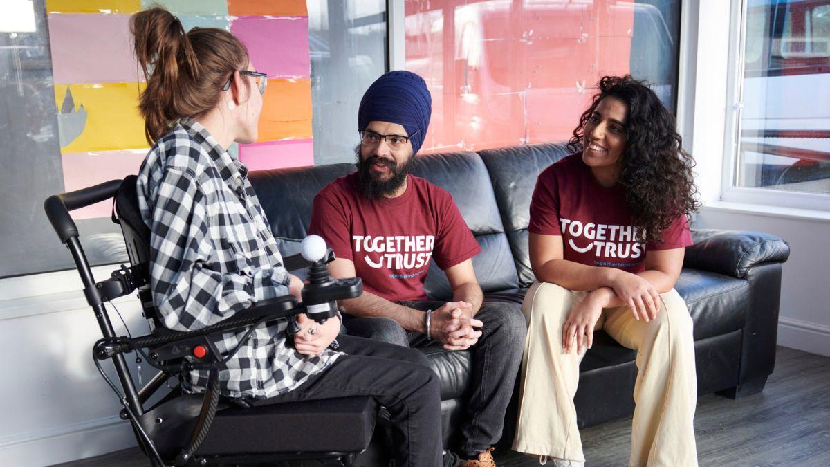 Two adults and a young lady in a wheelchair sitting and talking.