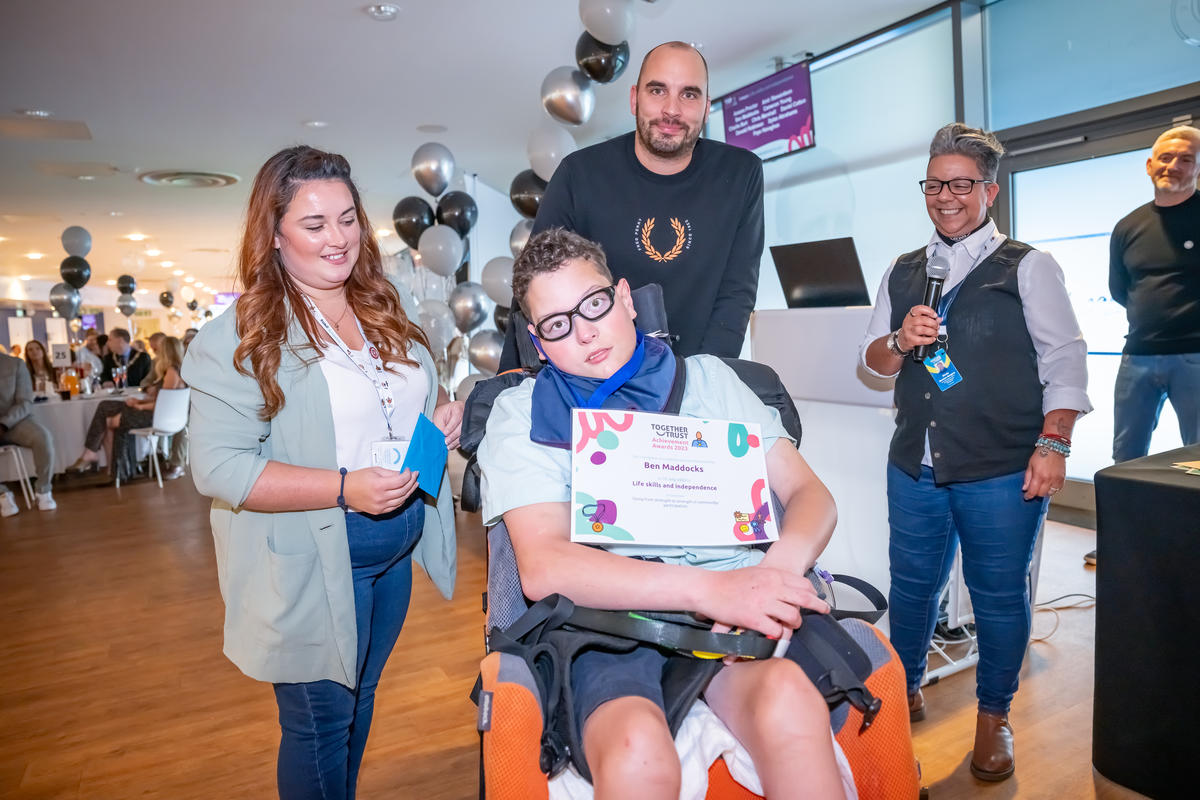 A young man in a wheelchair posing for a photo with his certificate between three staff members from the Together Trust