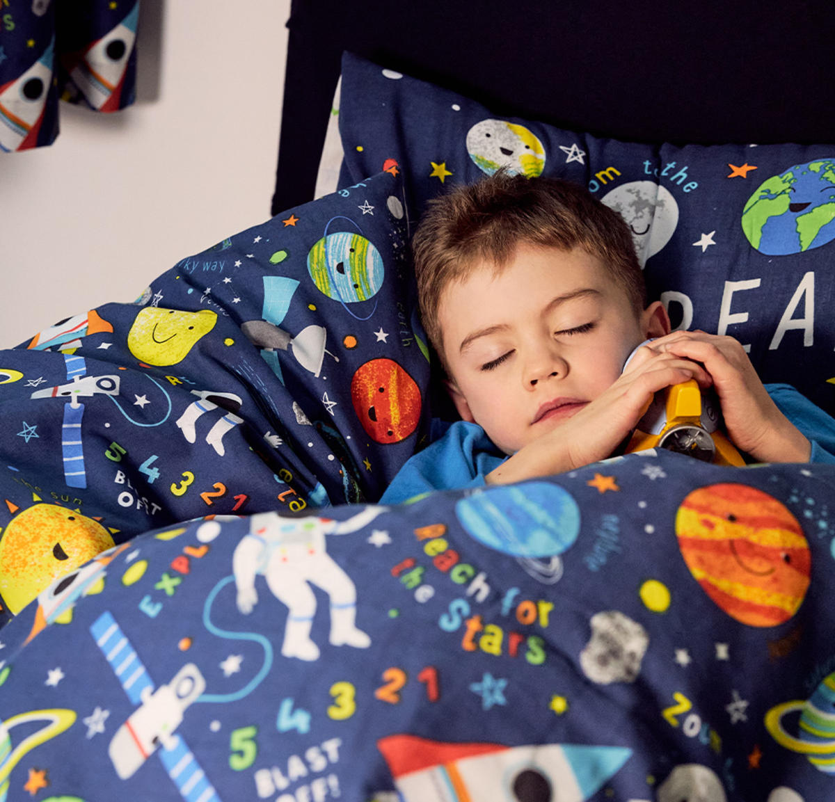 Young boy sleeping on a bed with space themed bedding. 