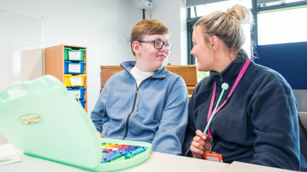 A Bridge College student sat at a table smiling at a member of teaching staff