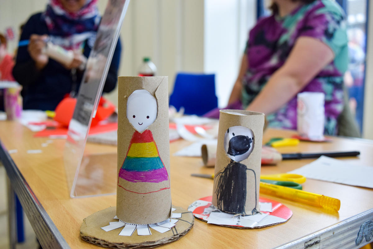 Two paper empathy dolls made from cardboard tubes with faces painted on. The left one is wearing a rainbow dress and is happy. The right one is dressed in black and looks surprised