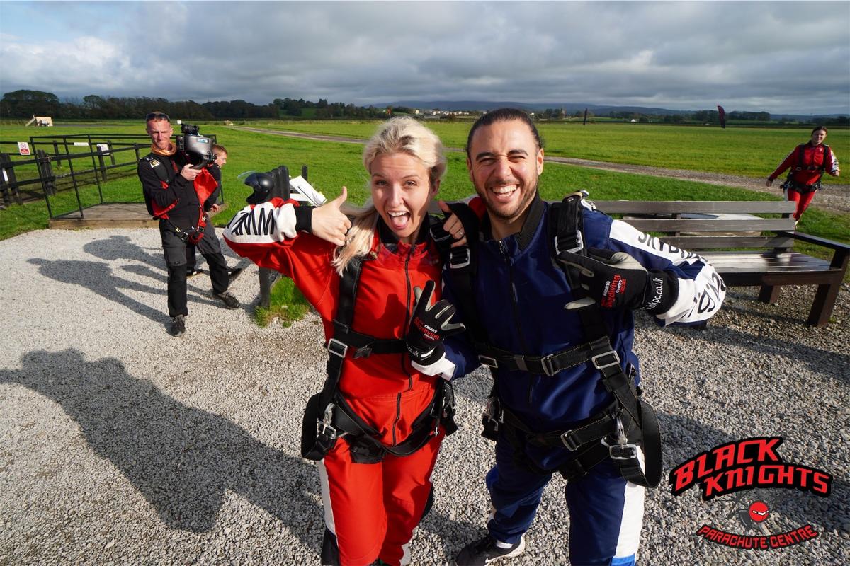 Two staff members smiling widely at the camera in their skydiving equipment