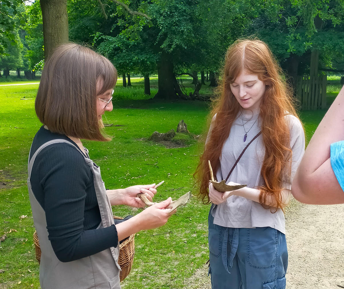 Young girl holding deer antlers. She is looking down smiling. Next to her is a staff member from Dunham Massey park explaining. They are stood outside in the park.