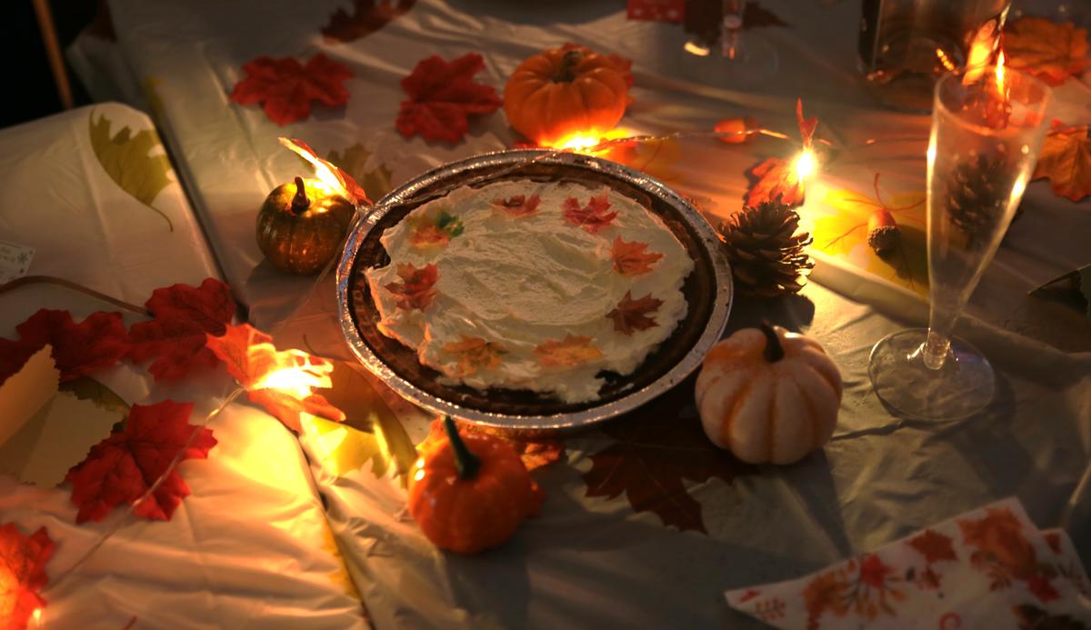 A pumpkin pie on a table decorated with autumn leaves and lights