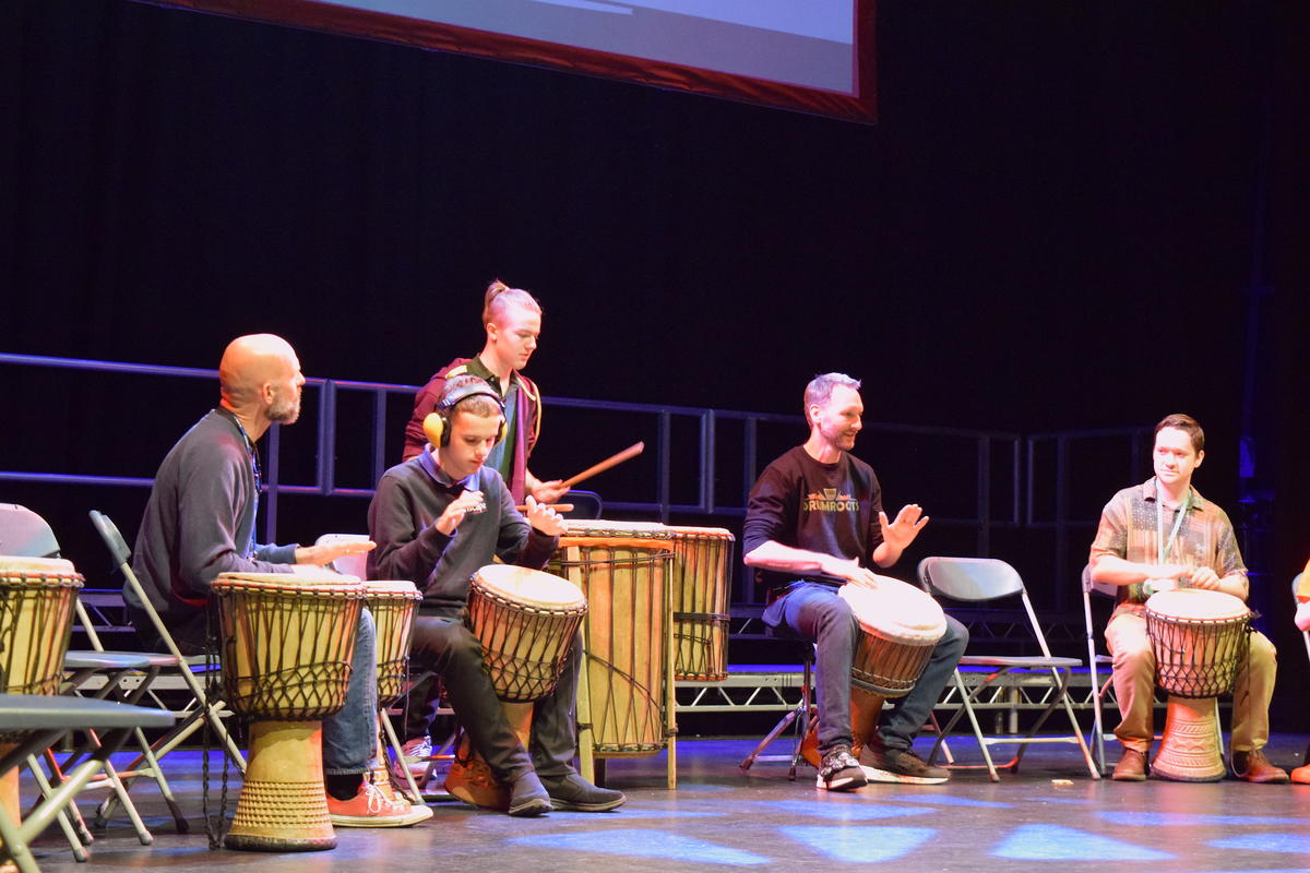 Students and staff in a row on stage. They are playing the drums.