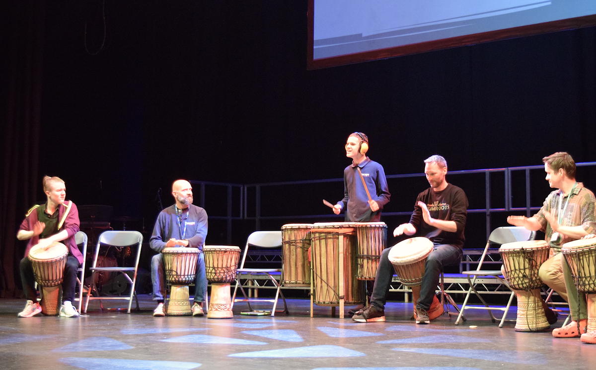 Students and staff in a row on stage. They are playing the drums.