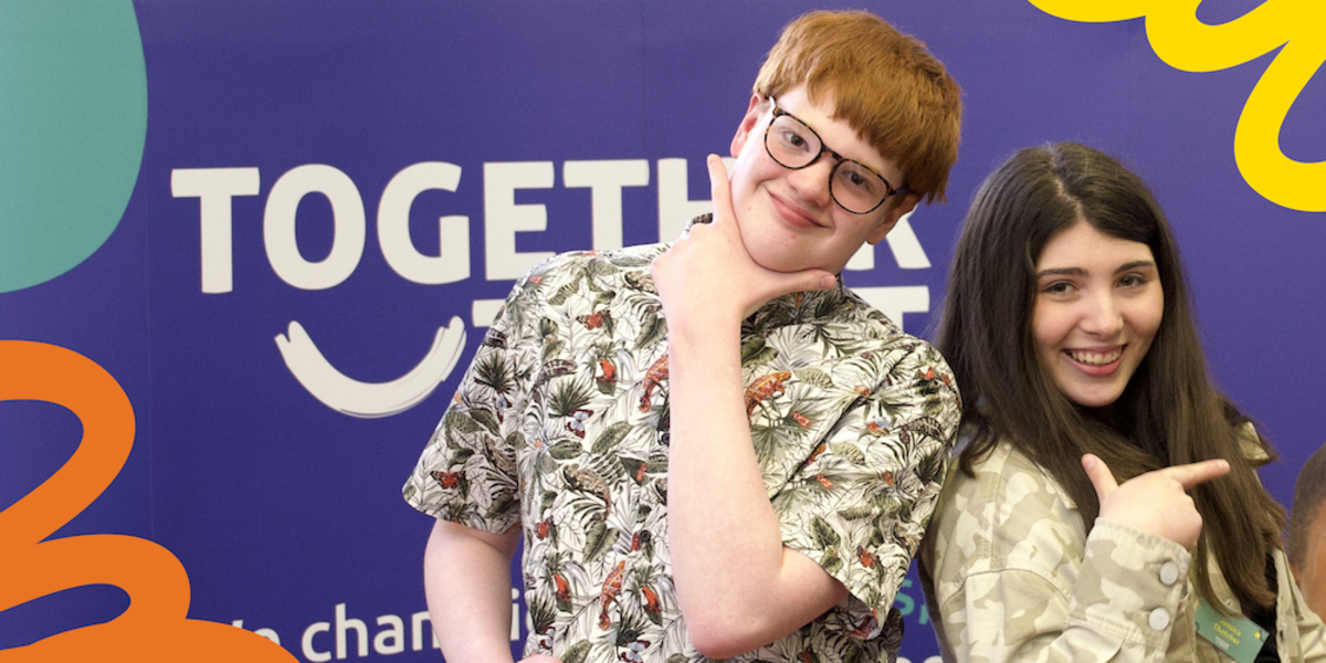 James and Jessica smile at camera behind blue Together Trust banner