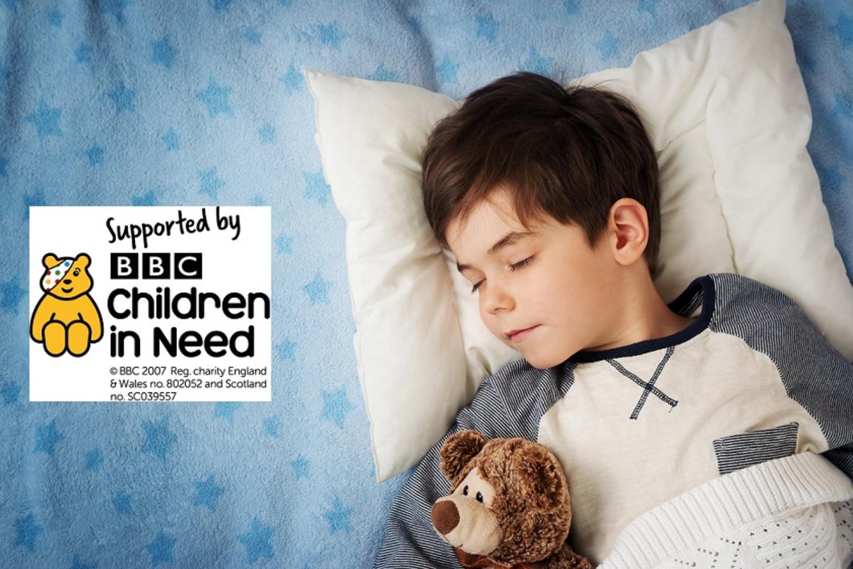 A boy sleeping with a teddy in bed with Children in Need logo