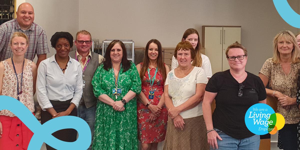 Together Trust staff stand in a group, facing camera and smiling. The Living Wage logo is on the bottom right.