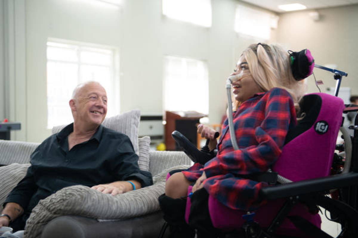 A woman sat in wheelchair talking to a man sat on a sofa A woman sat in wheelchair talking to a man sat on a sofa