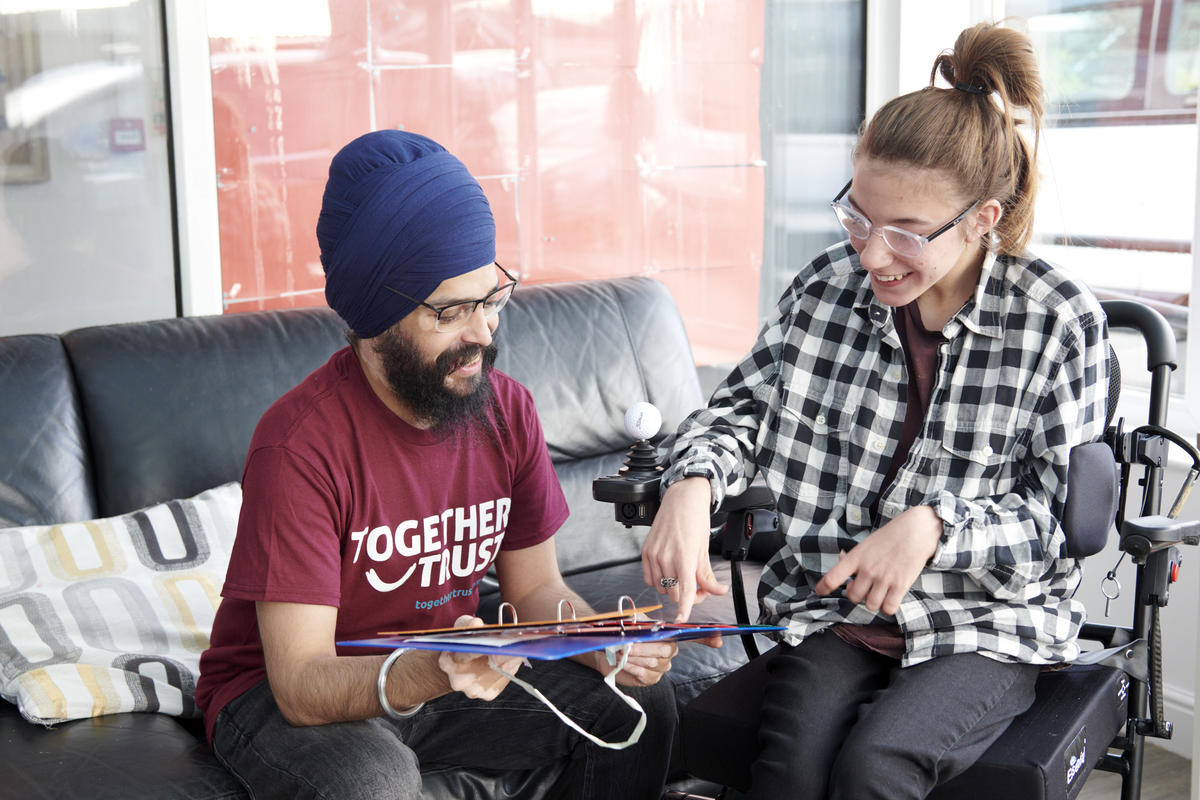 a staff member wearing a together trust t shirt showing a young woman in a wheelchair something on an iPad