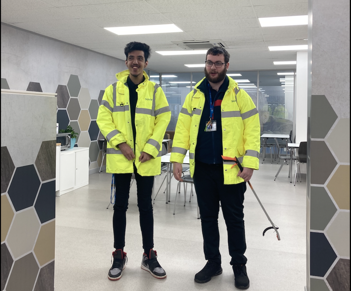 two students stood smiling wearing high vis jackets