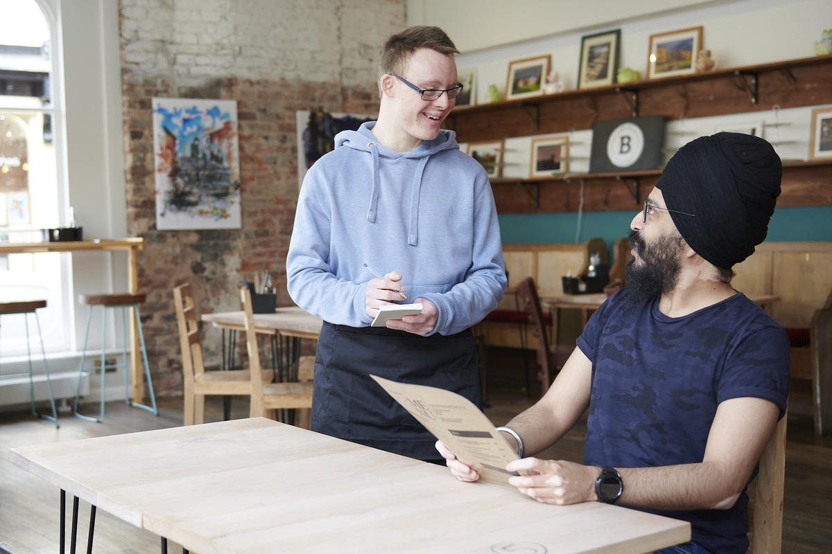 Young man with down syndrome taking a customer order in a coffee shop. 