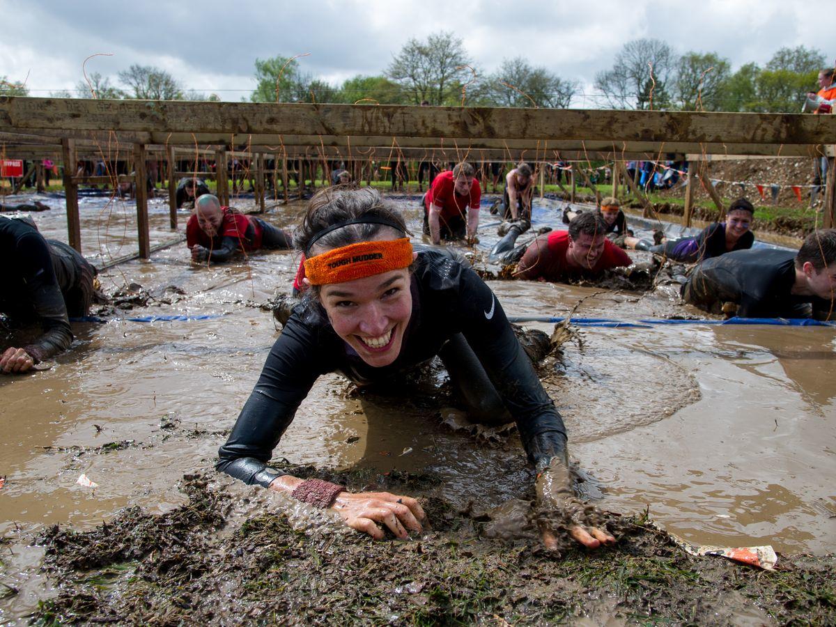 A participant in tough mudder crawling through mud towards the camera