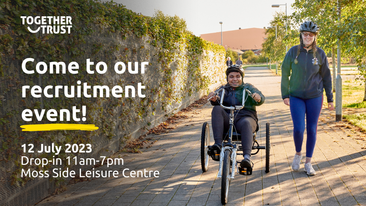 Young man on an accessible bike, smiling as he cycles along the road with a support worker.