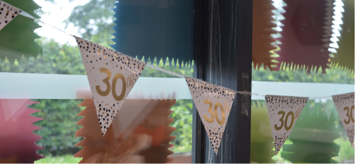 A photograph of bunting hung in front of a window. It's decorated with gold text "30th'