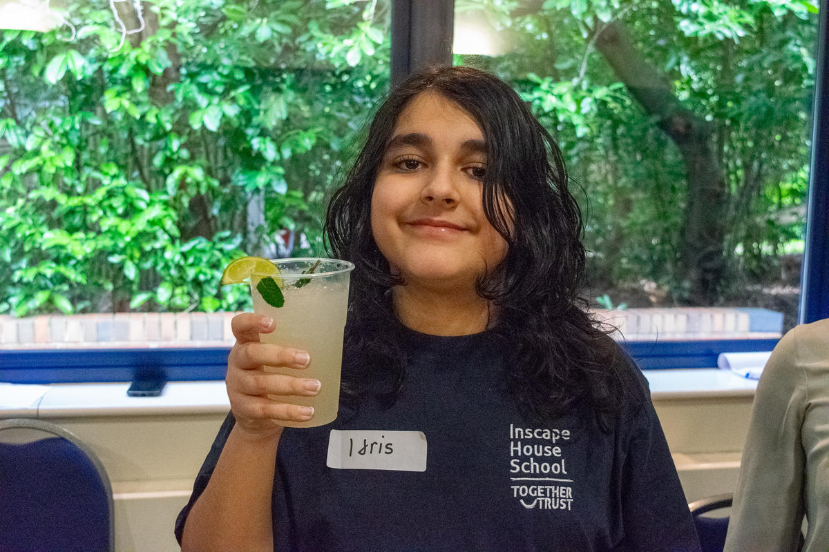 Young boy holding up a plastic cup. He is showing the alcohol-free mojito he made and smiling. 