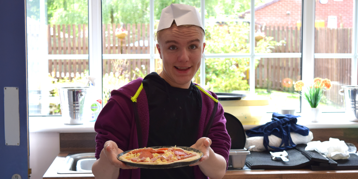 A student smiling while showing the pizza his pizza.