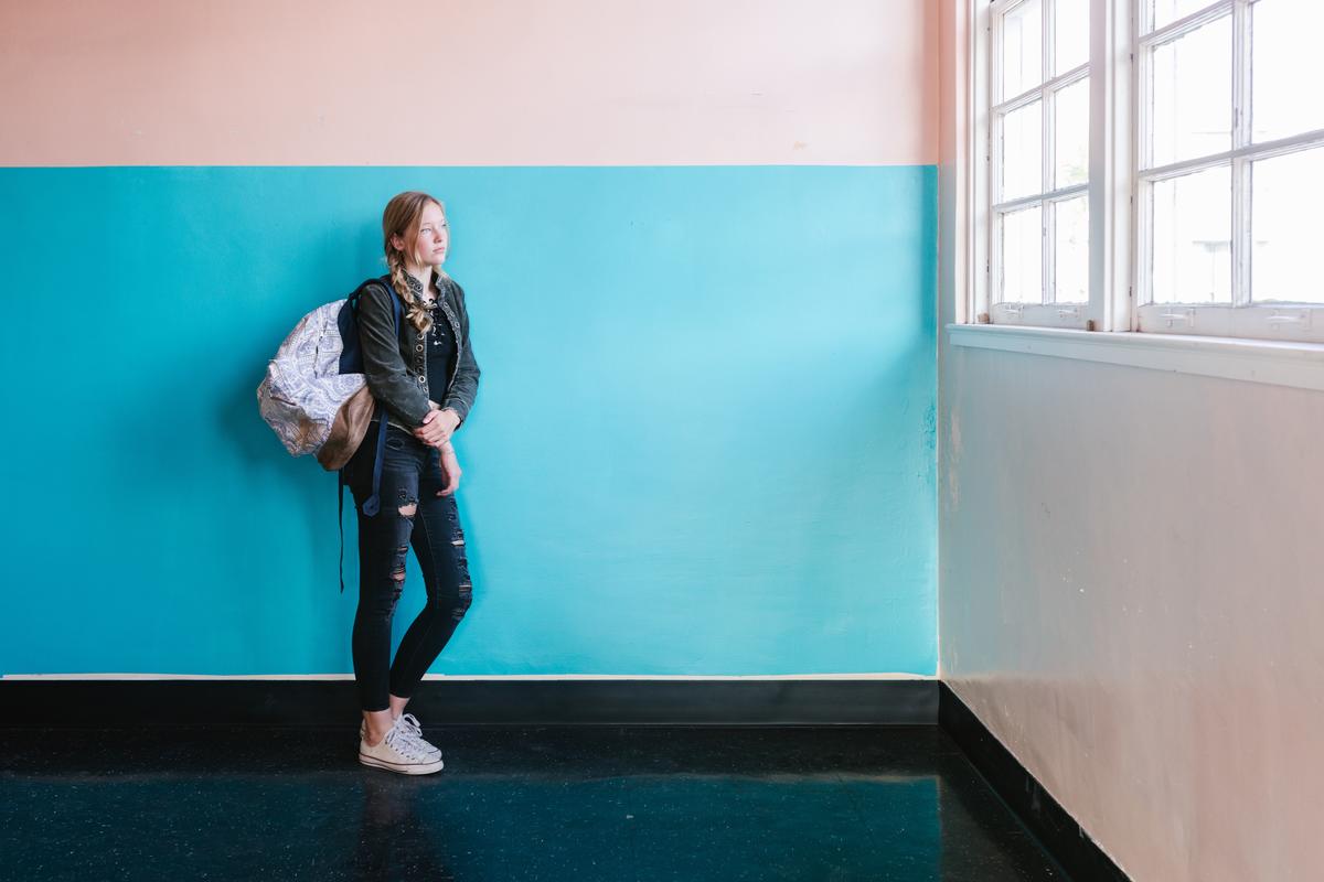 Young woman stands in front of a bright blue and white painted wall, looking out the window.