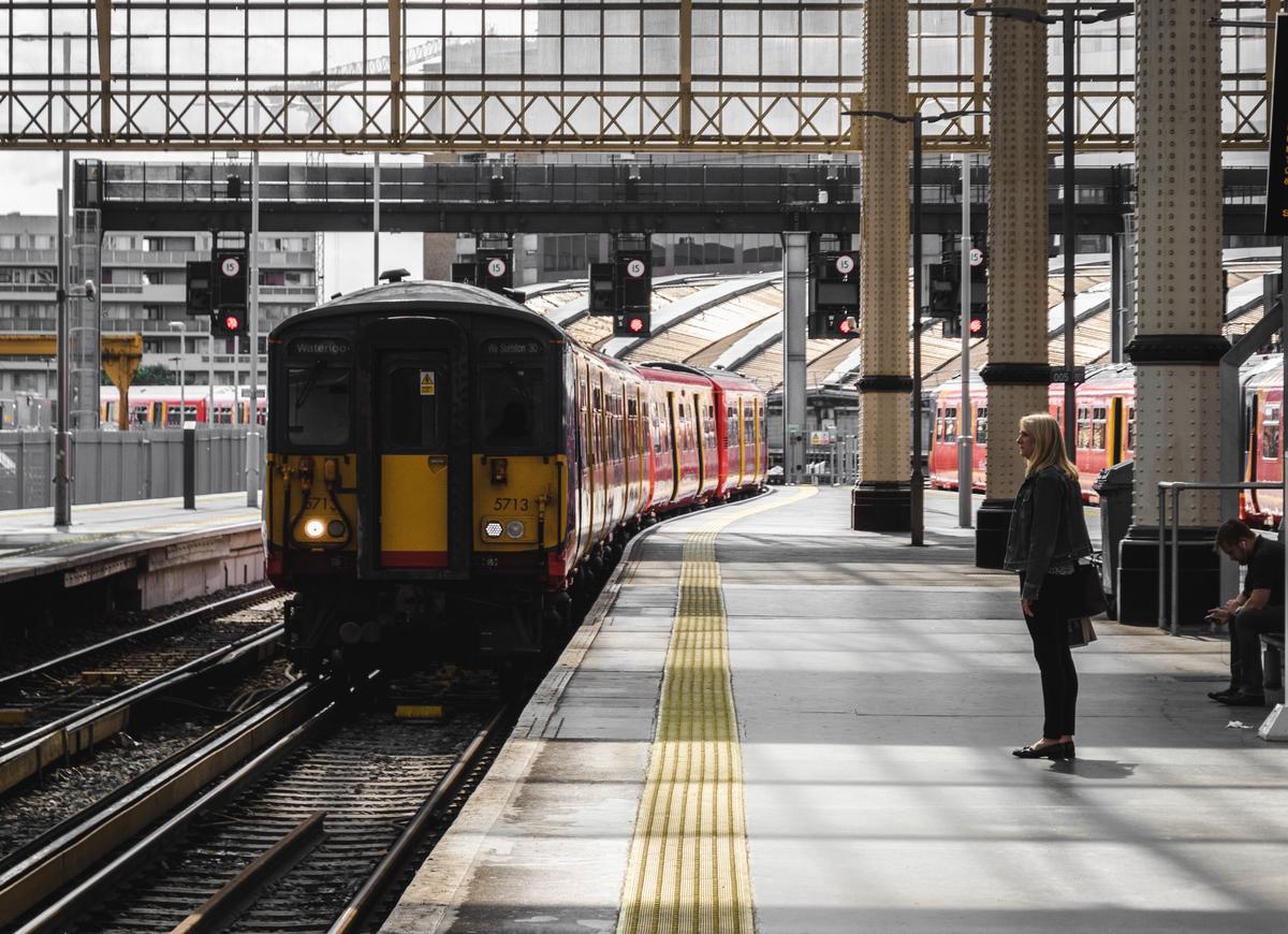 Person waiting behind the yellow line in on a train station platform. A train is approaching the platform. 