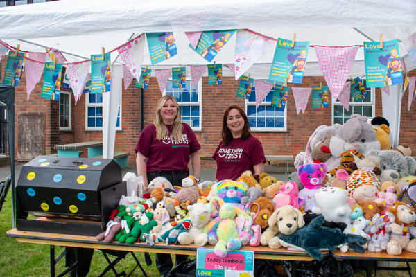 two people in purple together trust t shirts stood at a teddy bear stall at join together festival