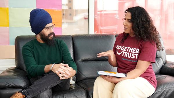 Two adults sitting on a couch and talking.