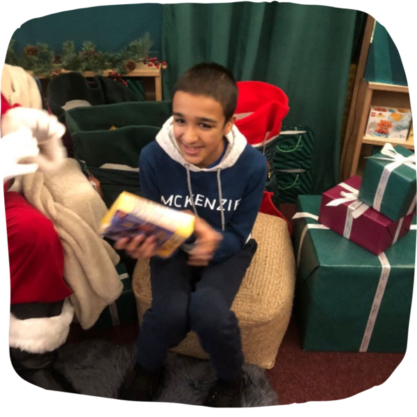 Young boy sitting down on a chair next to Father Christmas. He is holding a present and smiling. 
