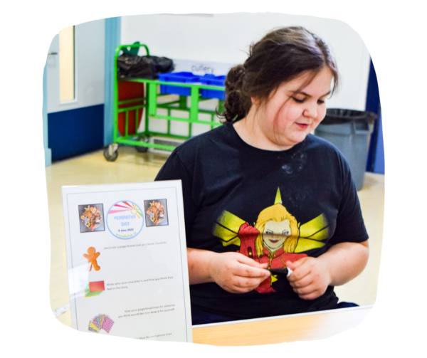 A young girl looking down smiling. She is holding a tube of sugar paste for decorating cookies. In front of her is a sign that says "Gingerbread decorating station. Empathy day" 