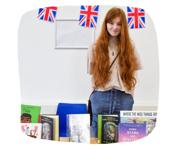 Talia at the book stall Talia, a young girl from Inscape House School standing in front of a table full of books. she is smiling at the camera
